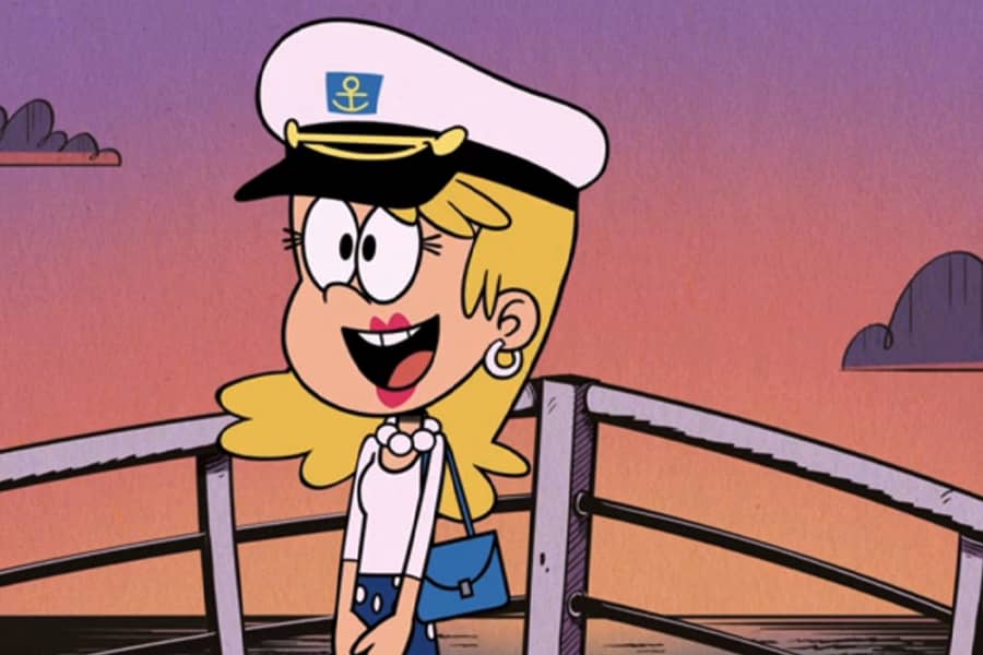 blonde woman at the bow of a boat wearing a captain’s hat
